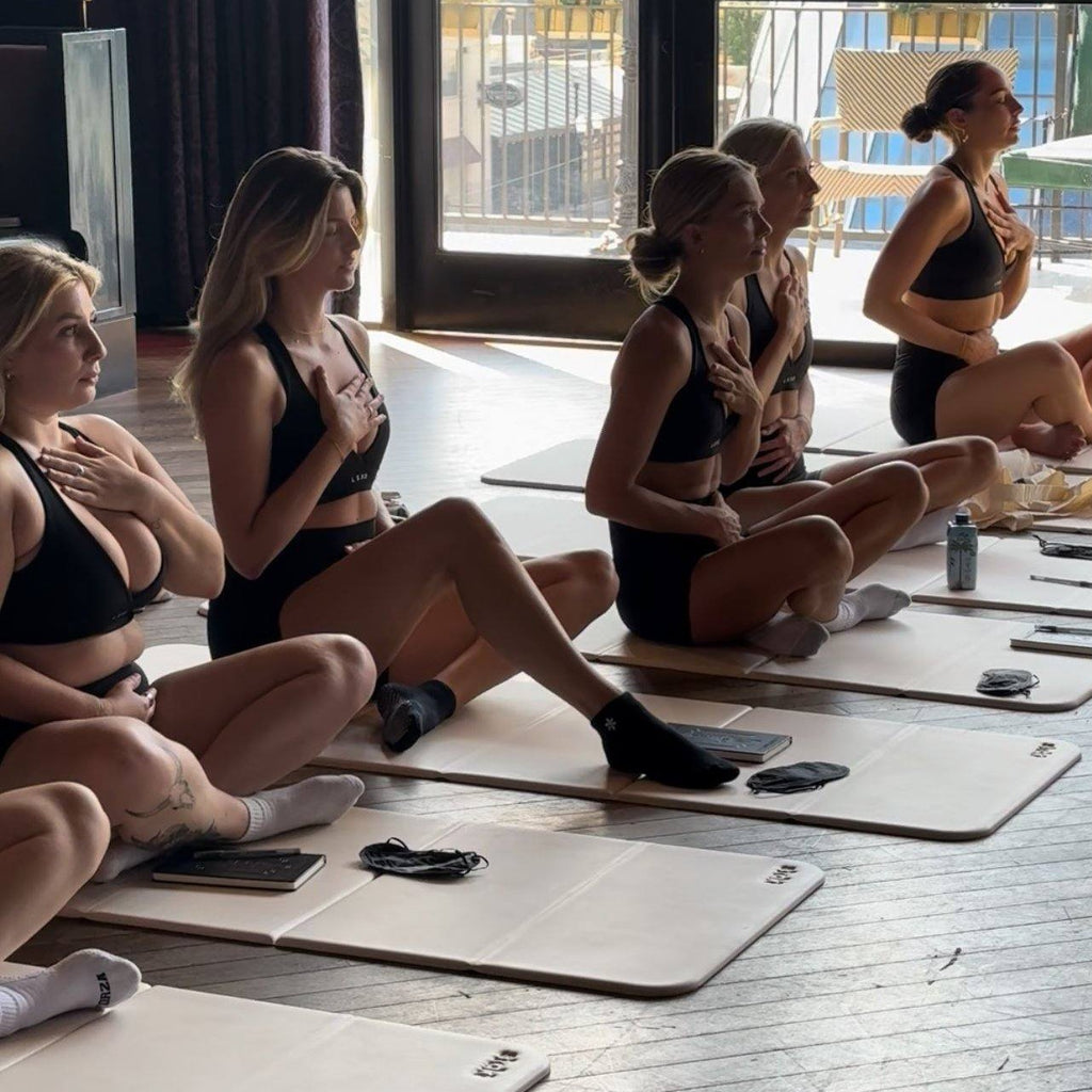 A class seated on mats with hands on their hearts in morning light
