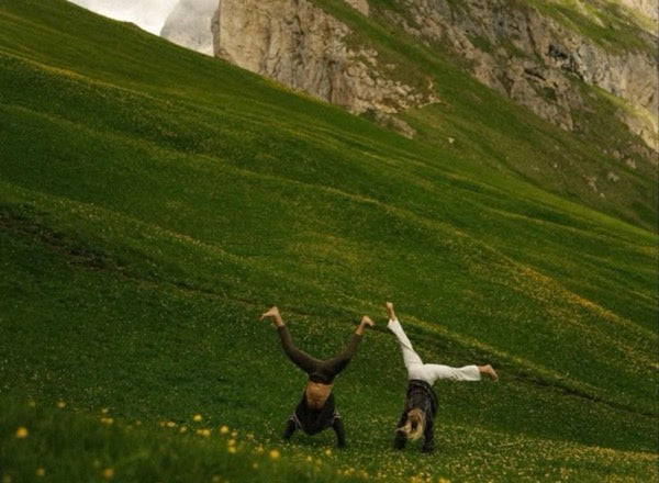 Two people upside down on a green mountain hillside